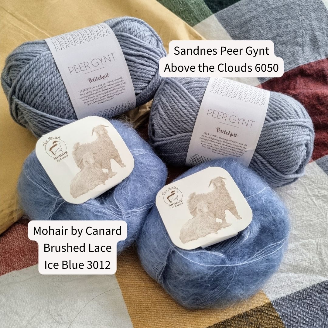 The picture shows two balls of Sandnes Peer Gynt wool yarn in the colour Above the Clouds, a light-mid dusty blue colour, next to two balls of fluffy silk mohair yarn called Brushed Lace by Mohair by Canard in the colour Ice Blue, a light-mid blue colour, the colour is very similar and a little brighter than the Peer Gynt. The fluffy yarn has a square label on top with a picture of two hairy goats. All four balls of yarn are sitting on top of a checkered sheet in white, yellow, red, green and blue.