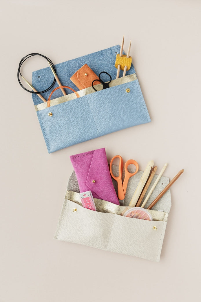 Two leather pouches with knitting needles and haberdashery items on a light background