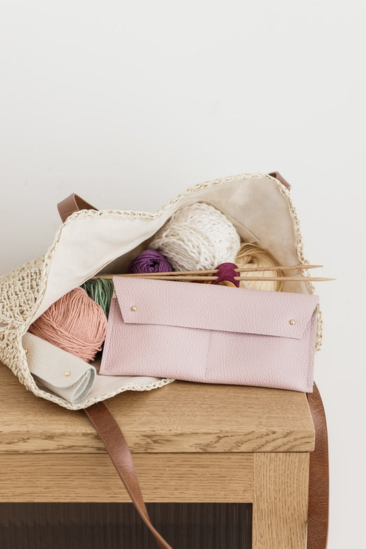 Pink leather notions pouch displayed with yarn and knitting needles on a wooden surface